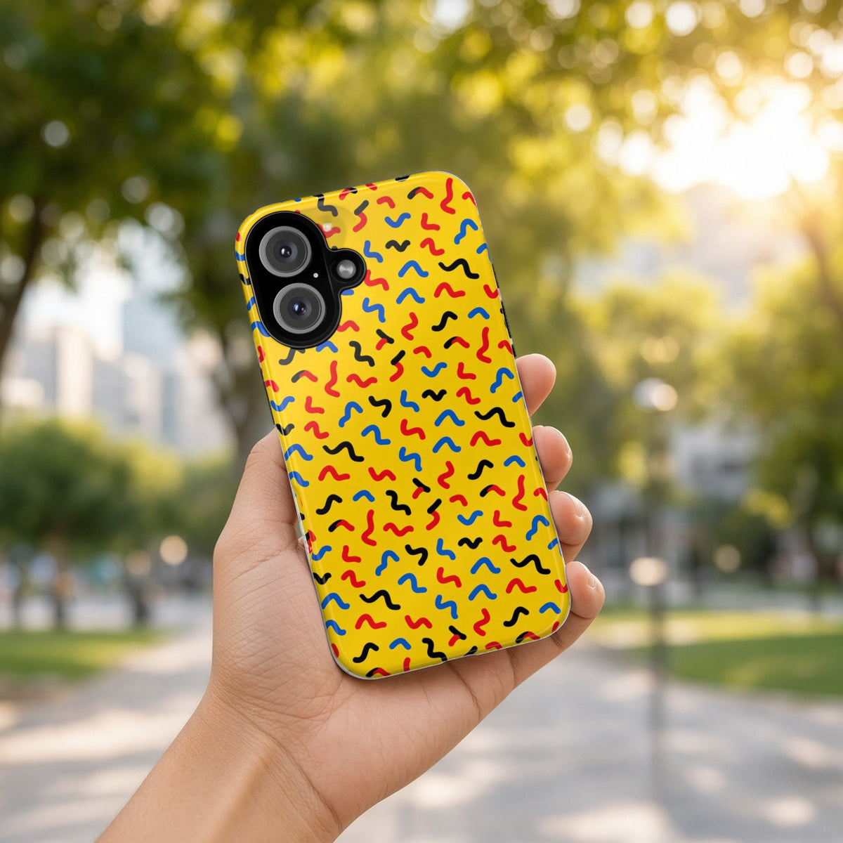 Hand holding the Squiggle Strokes Yellow tough phone case outdoors in a sunny park