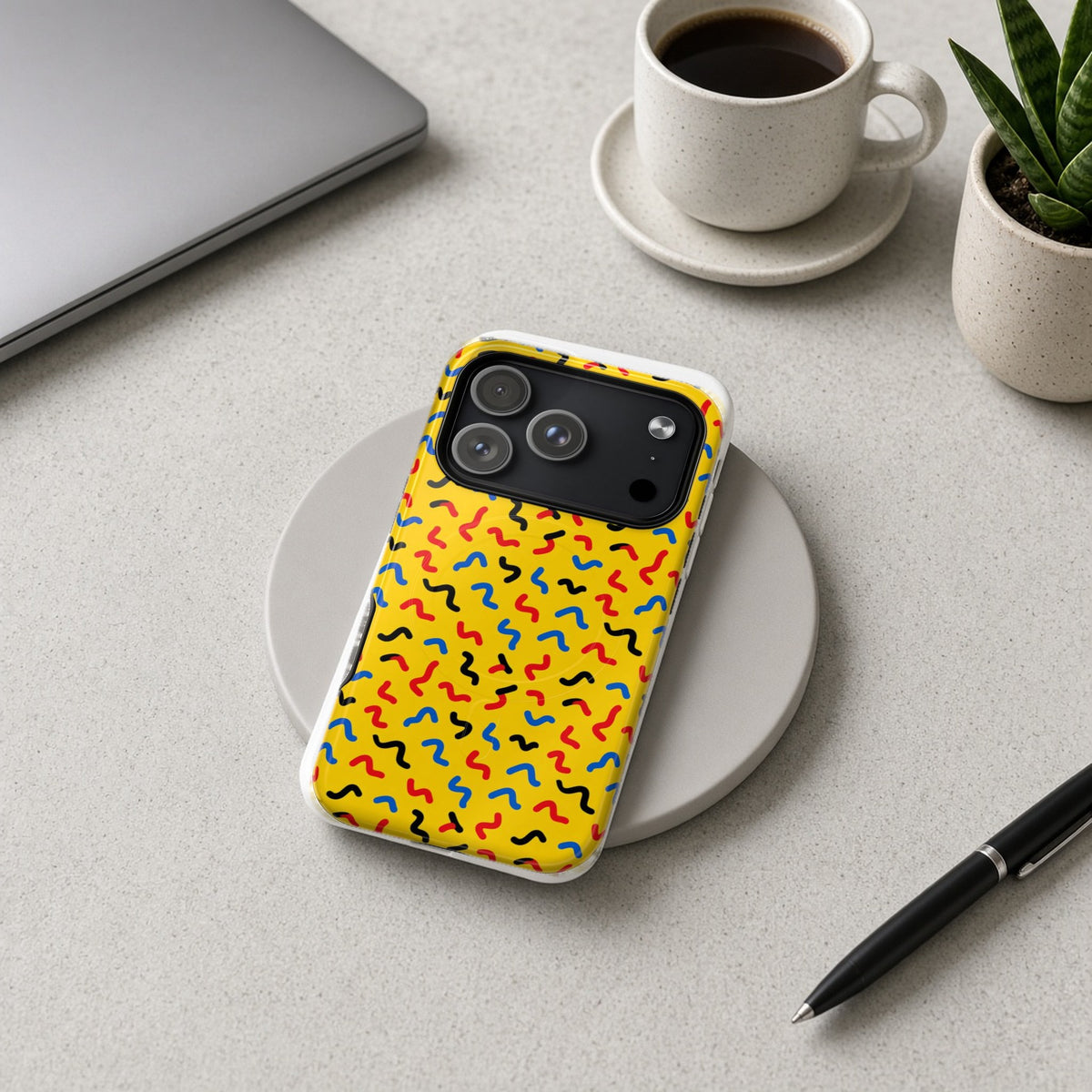 Squiggle Strokes Yellow magnetic iPhone case on a wireless charging pad on a grey desk