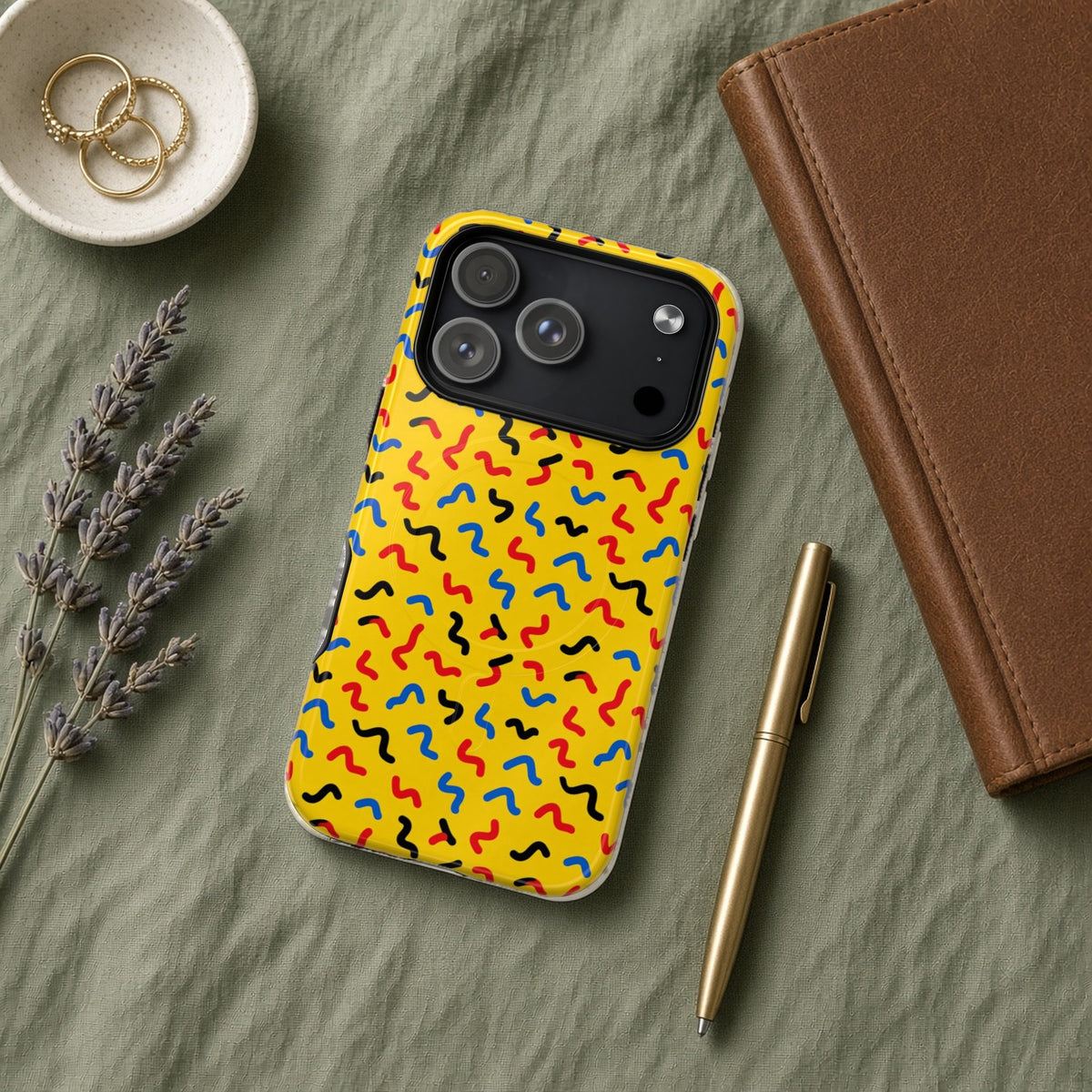Squiggle Strokes Yellow magnetic iPhone case flat lay on sage linen with a notebook and pen
