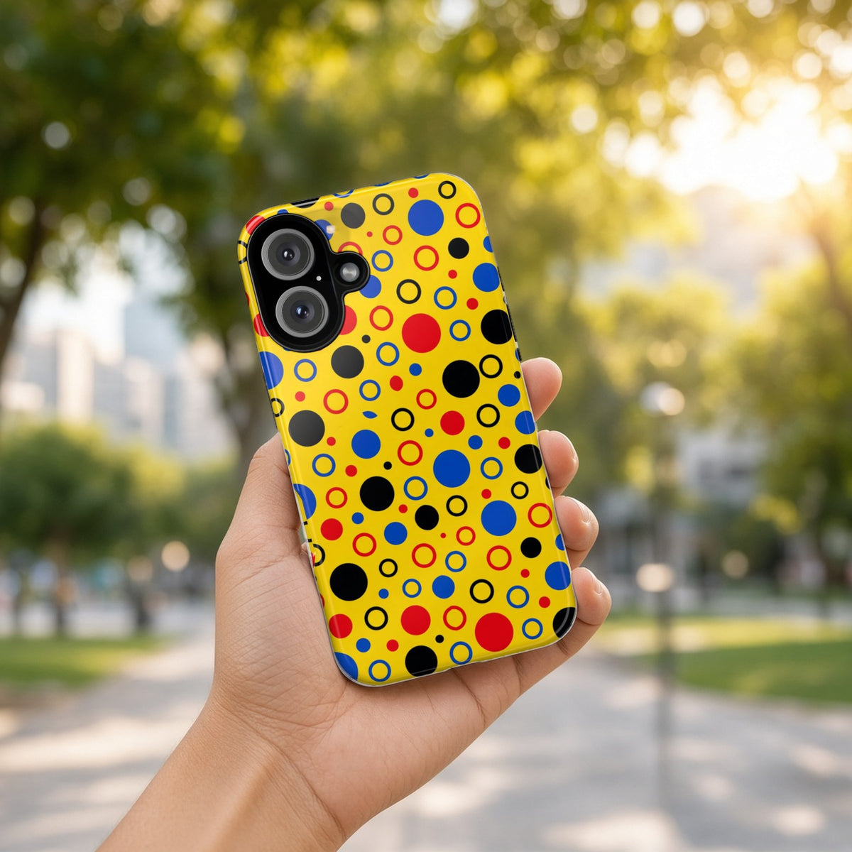 Hand holding the Bubble Outlines tough phone case outdoors in a sunny park