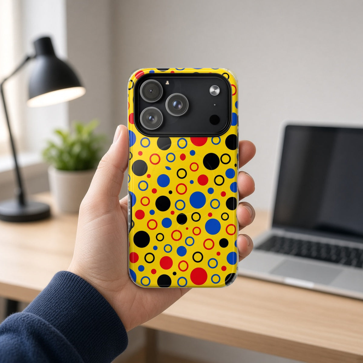 Hand holding the Bubble Outlines magnetic iPhone case at a home office desk